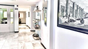 A hallway with a tiled floor, framed artwork on the wall, and a door with a frosted glass window. - Arriadh (Córdoba)