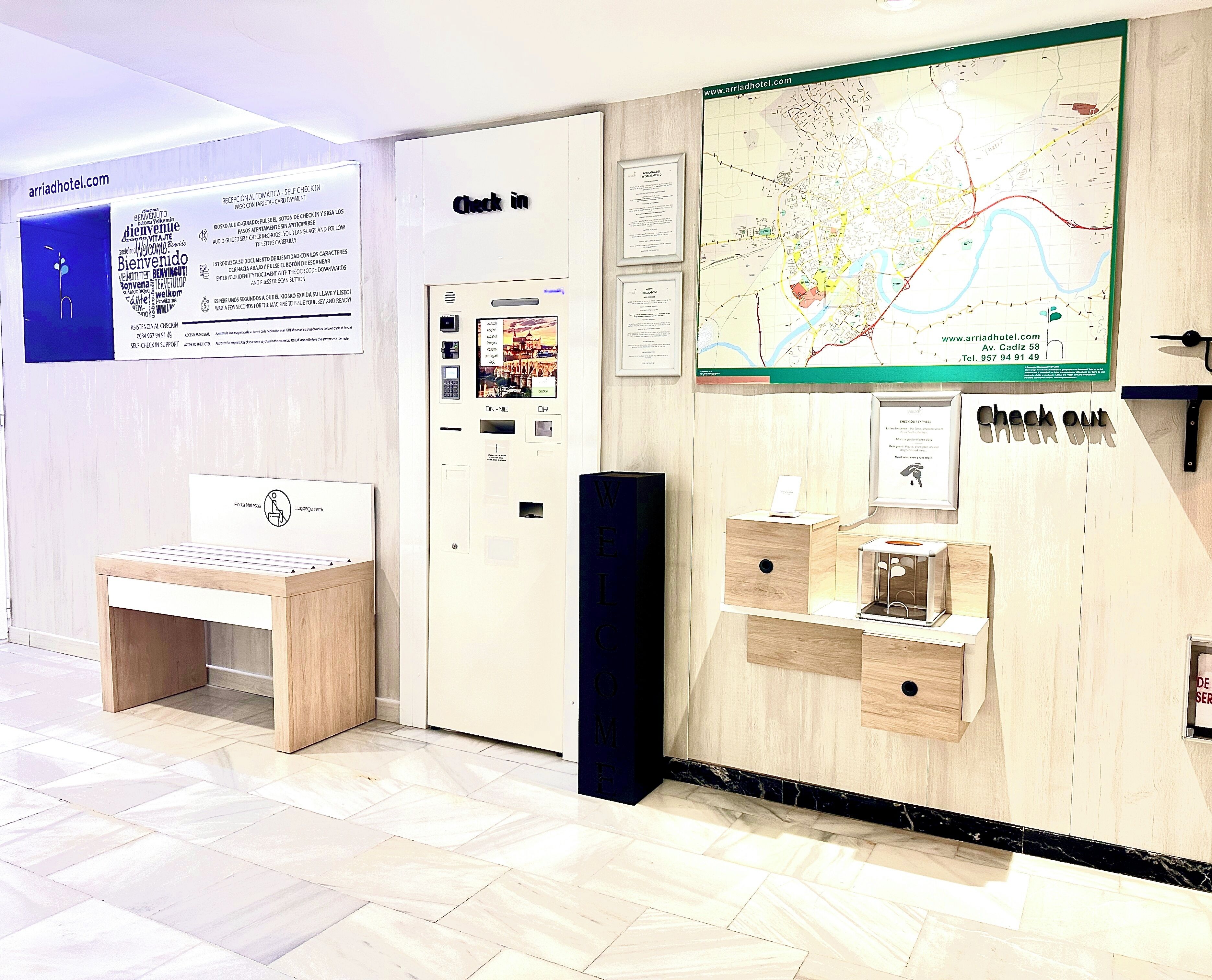 Una zona de recepción con un quiosco de auto-registro, un perchero para equipaje y un mapa en la pared.
