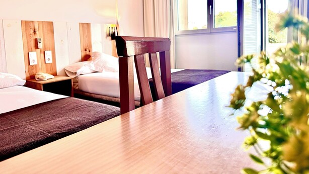 A hotel room with two beds, a wooden table, and a window with curtains. - Arriadh (Córdoba)