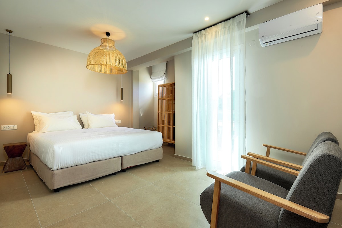A bedroom with a bed, bedside tables, a chair, a hanging light fixture, and an air conditioning unit.