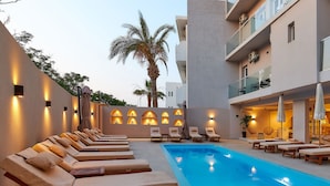 A poolside area with sun loungers, a swimming pool, and a building with balconies. - Lotus Rise Hotel (Hersonissos)