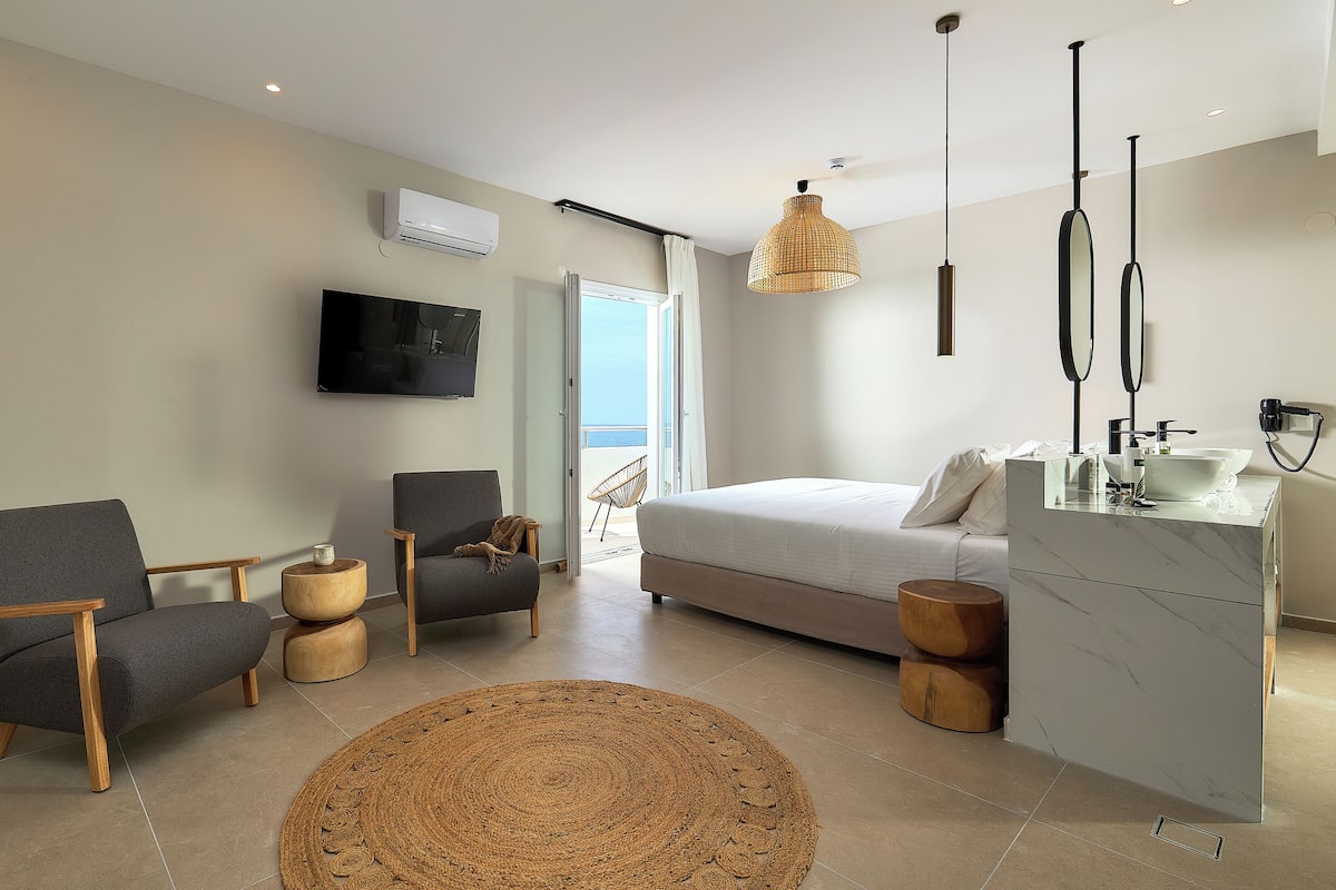 A modern bedroom with a bed, a TV, a desk, and a balcony.