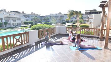 A rooftop yoga area with a pool view, wooden railings, and a clear sky.