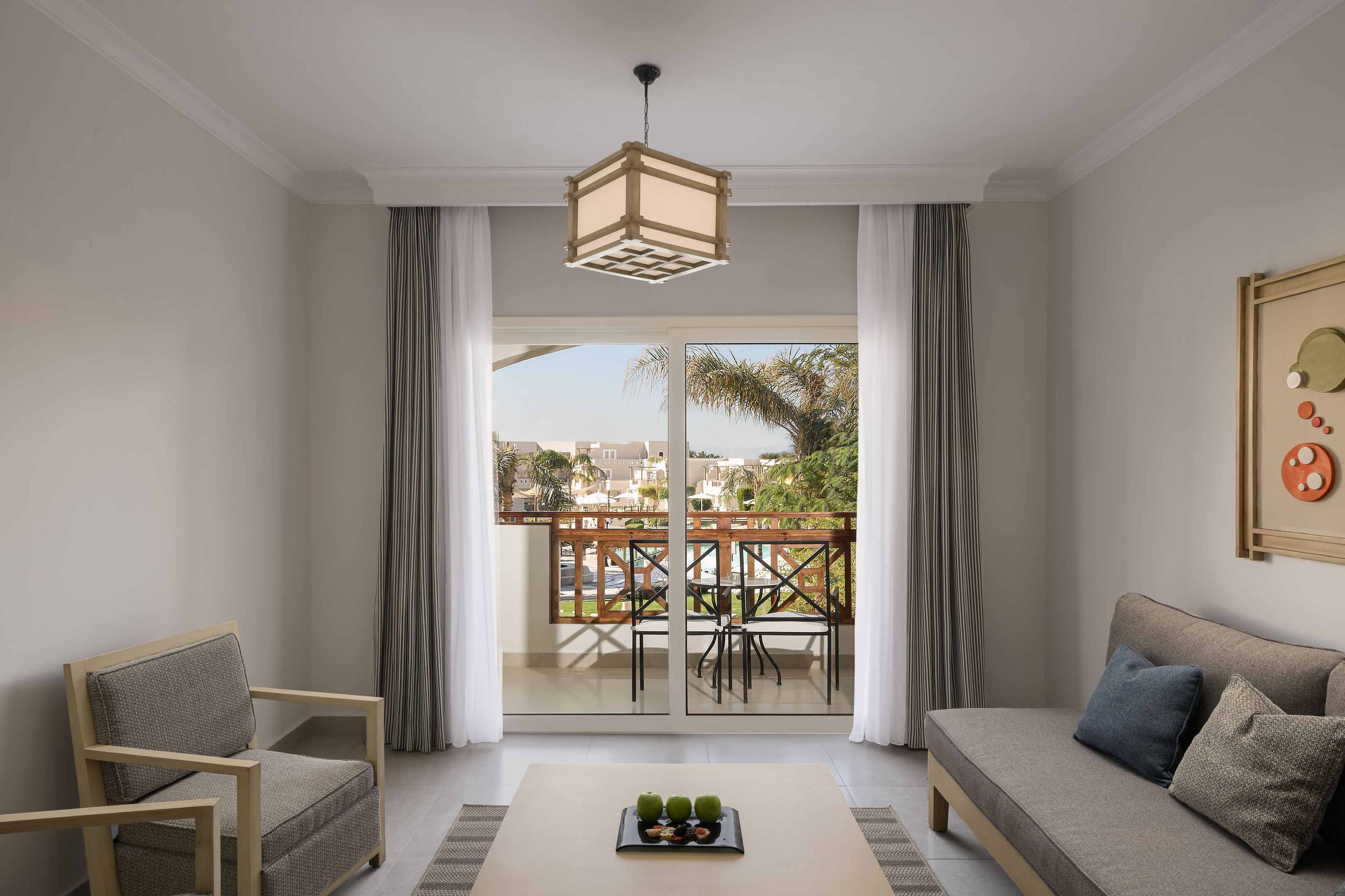 Ein Wohnzimmer mit einer Couch, einem Sessel und einem Tisch mit Früchten. Ein Balkon bietet Blick auf die Stadt.