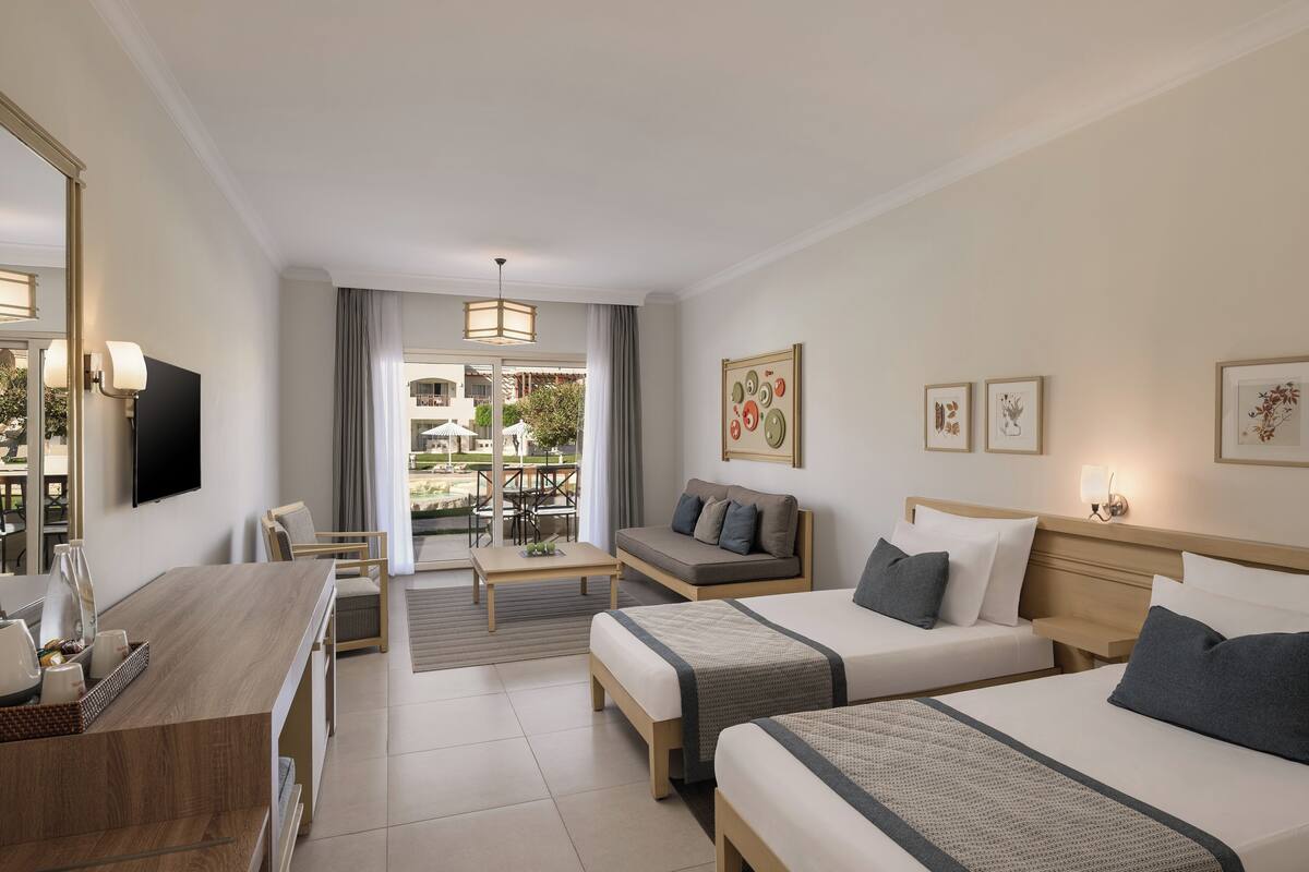 A hotel room with two beds, a desk, a sofa, and a dining area with a view of the outdoors.
