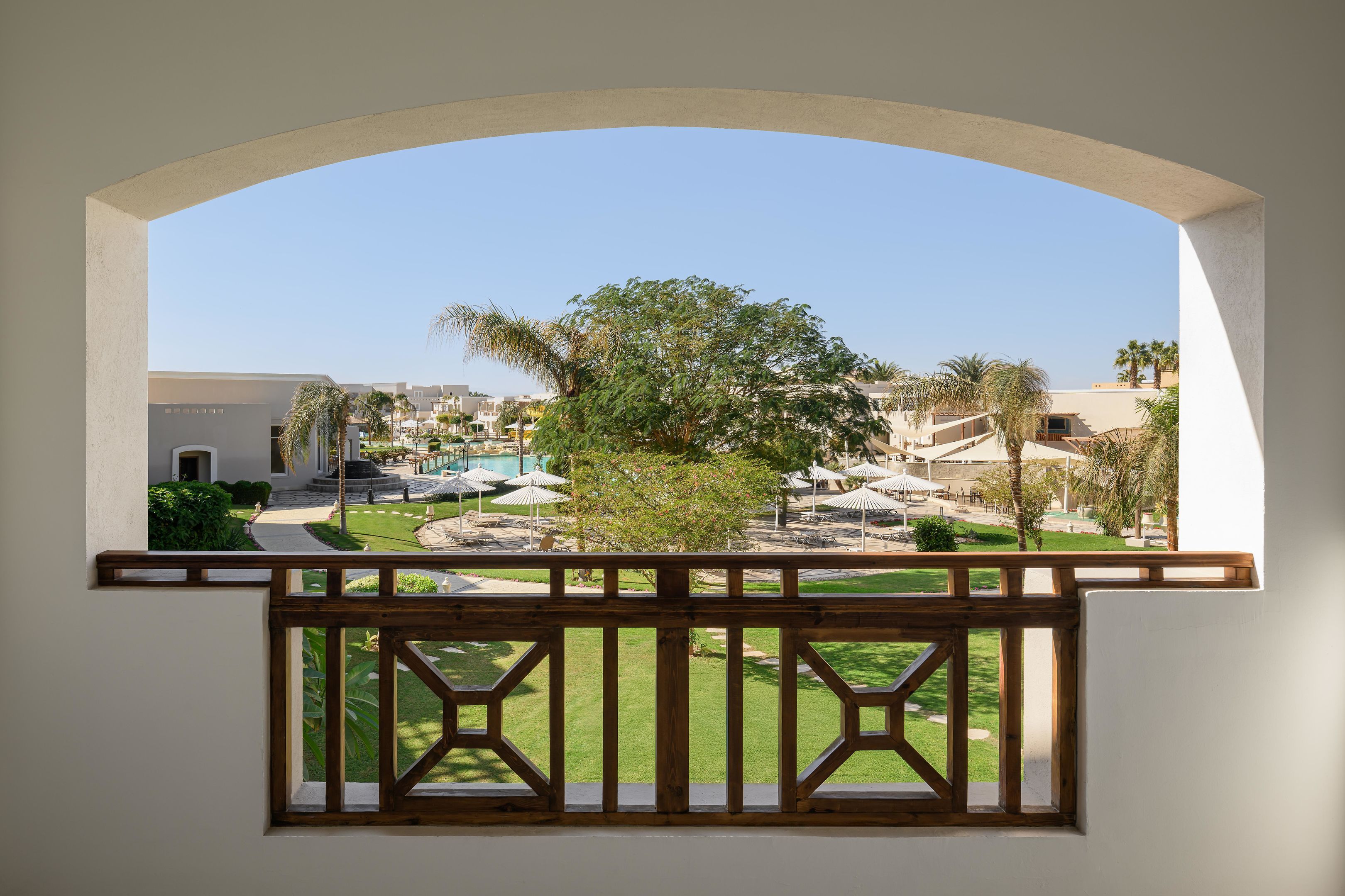 Ein Balkon mit Blick auf einen Poolbereich, Palmen und ein Gebäude mit weißer Fassade.
