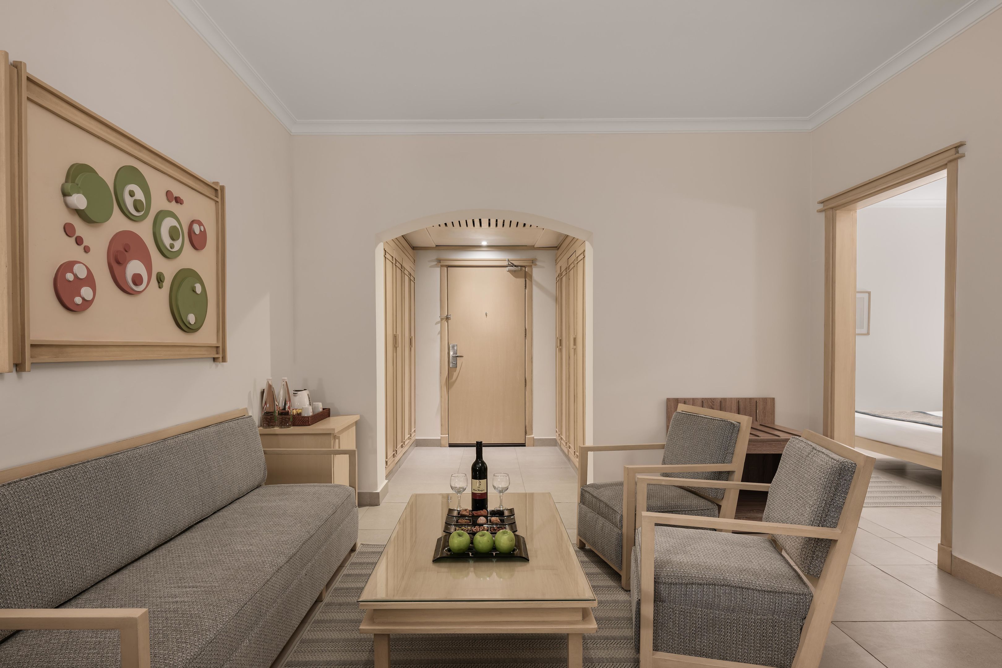 Un salon moderne avec un canapé, deux fauteuils, une table basse sur laquelle se trouvent une bouteille et des verres, et une œuvre d’art murale.