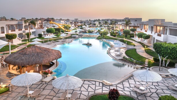 Um resort com piscina central, áreas de estar com guarda-sóis e um toboágua.