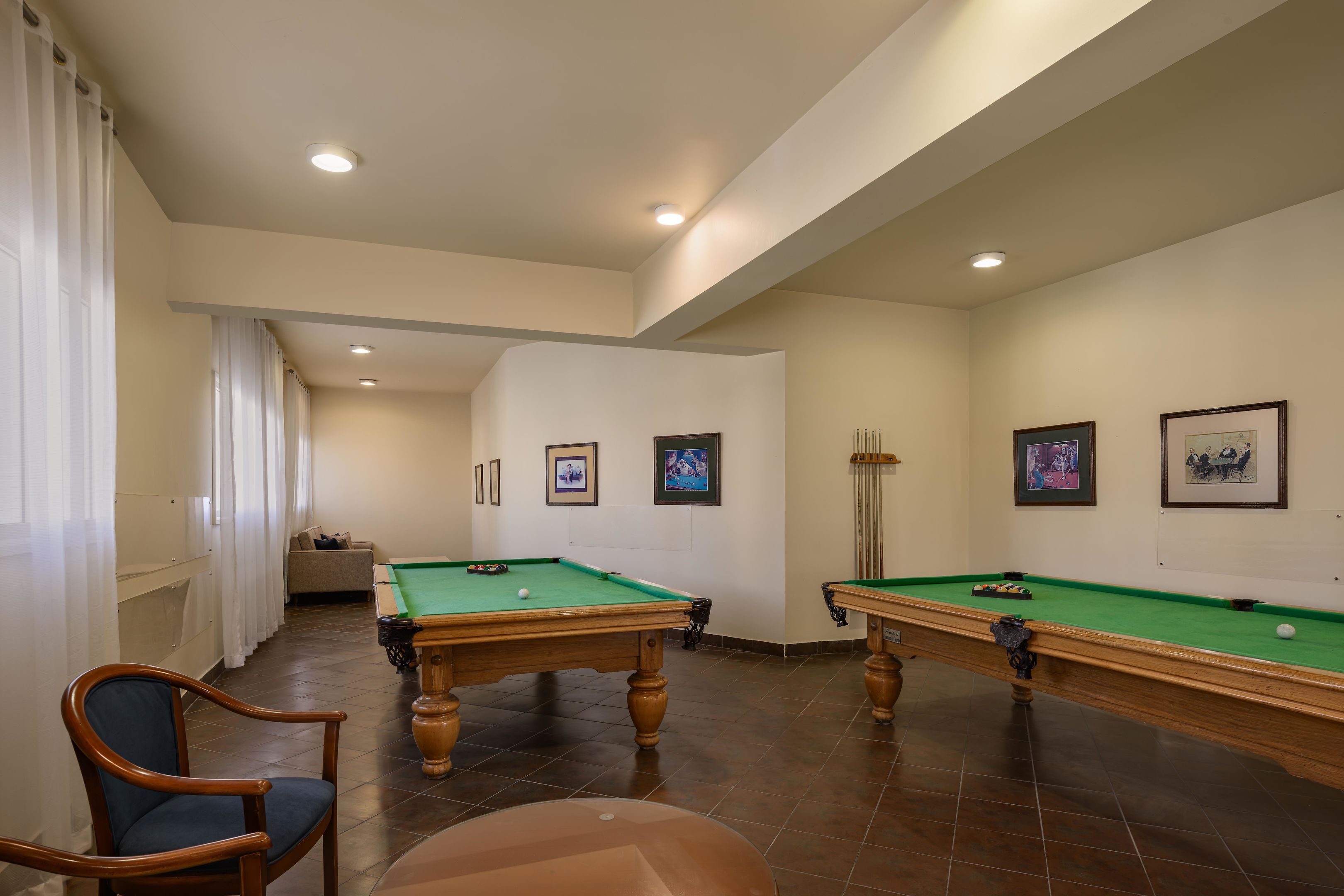 A pool table, a chair, and a billiards rack in a room with white walls and recessed lighting.