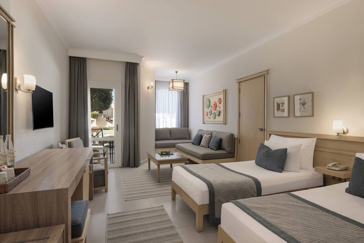A hotel room with two beds, a sofa, a desk, and a TV.