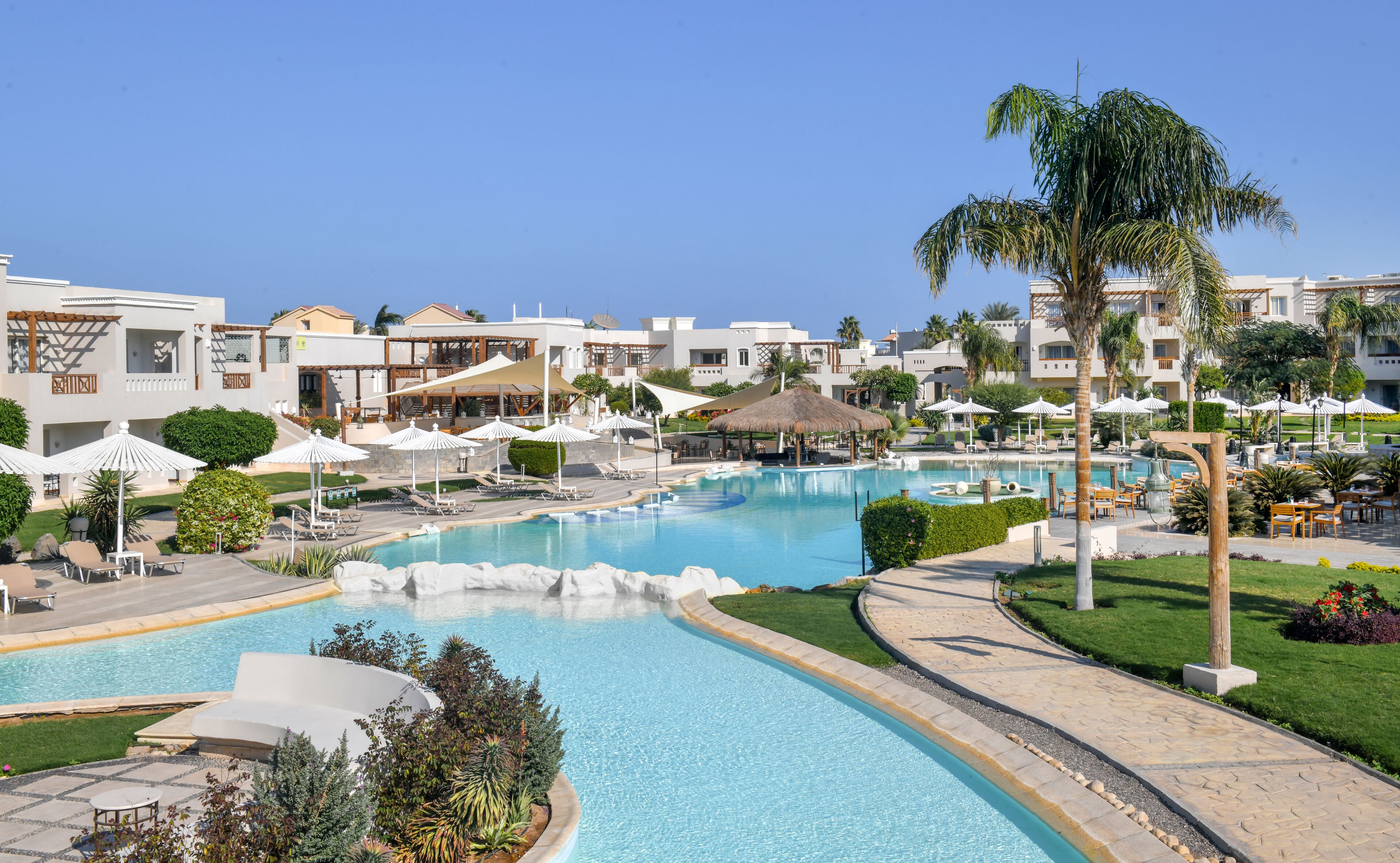 A resort with a large central pool, multiple lounge areas, and a variety of outdoor seating arrangements.