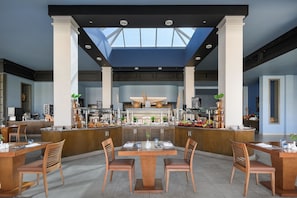 Restaurante moderno com ilha central, cadeiras de madeira e teto alto com claraboias.