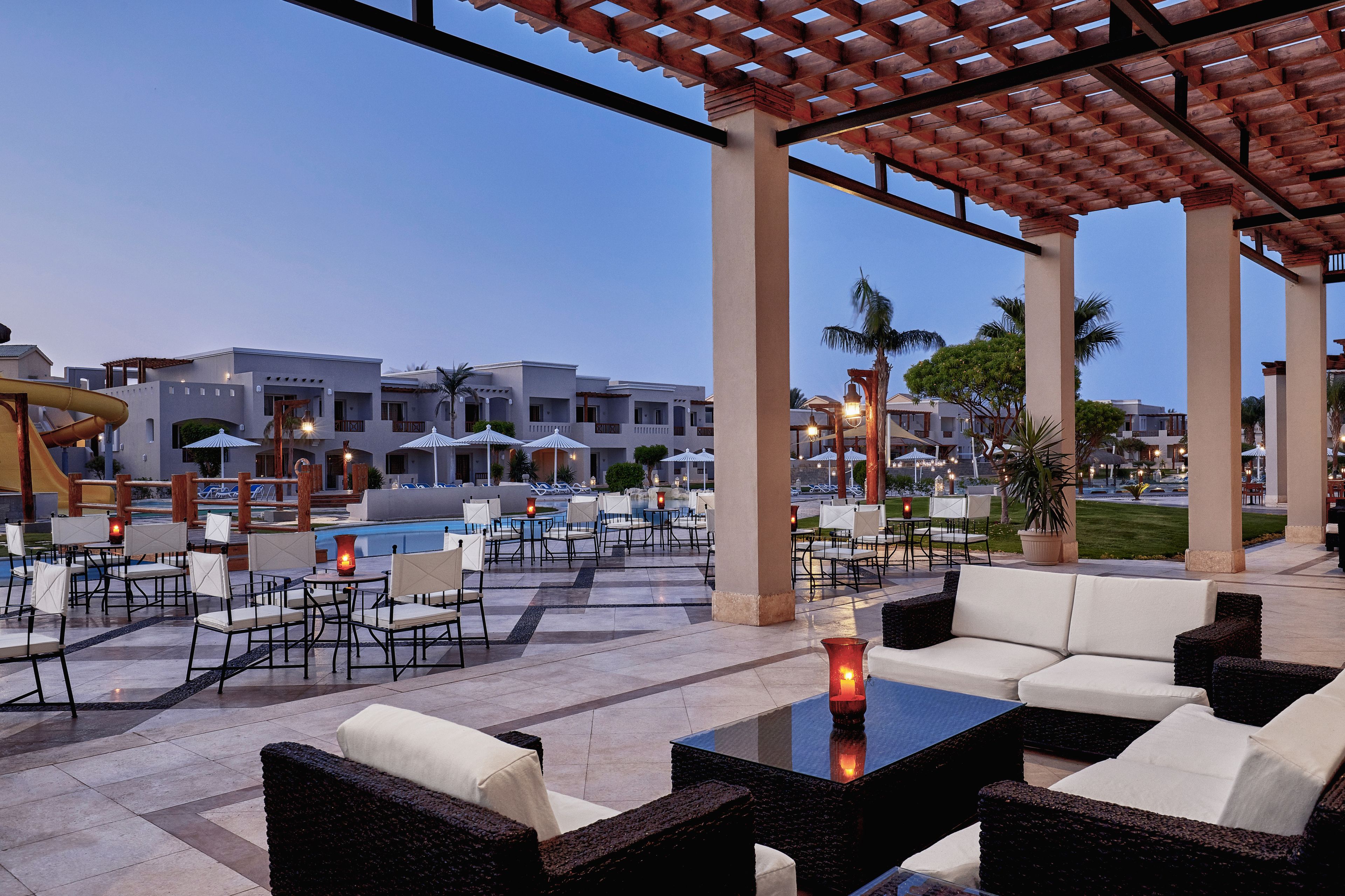 Ein Außen-Loungebereich mit Sitzgelegenheiten und Pool, inklusive Pergola und Palmen.