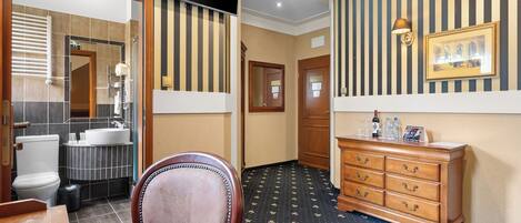 Quarto de hotel com banheiro, penteadeira de madeira, espelho e tapete estampado.