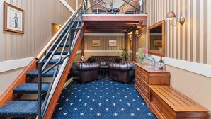 Una escalera con barandilla de madera que conduce a una zona elevada con asientos de cuero y un banco de madera.