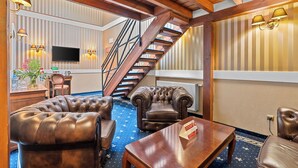 Un vestíbulo de hotel con una escalera, sofás de cuero, una mesa de centro de madera y lámparas fijadas a la pared.