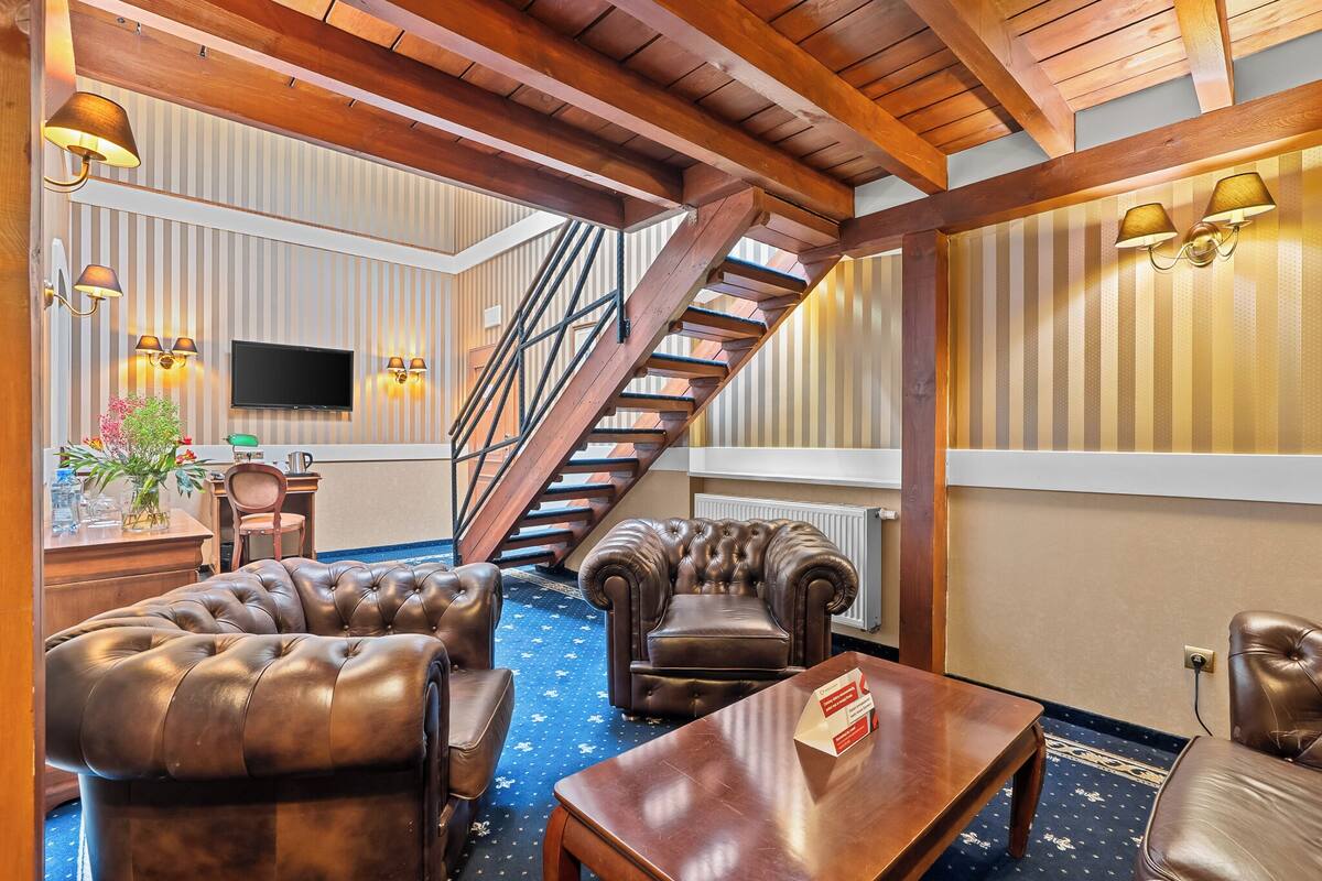 A hotel lobby with a staircase, leather sofas, a wooden coffee table, and wall-mounted lamps.