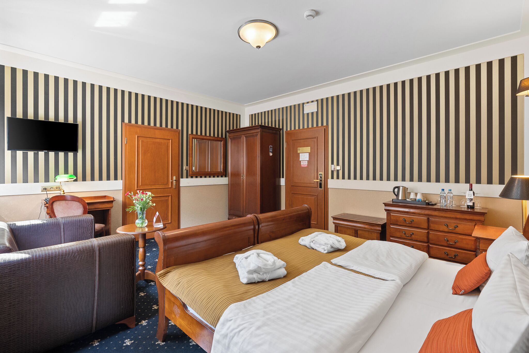 Habitación de hotel con una cama grande, un escritorio, una silla, un televisor y un armario.