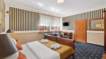 A hotel room with a bed, a desk, a chair, a TV, and a wardrobe.