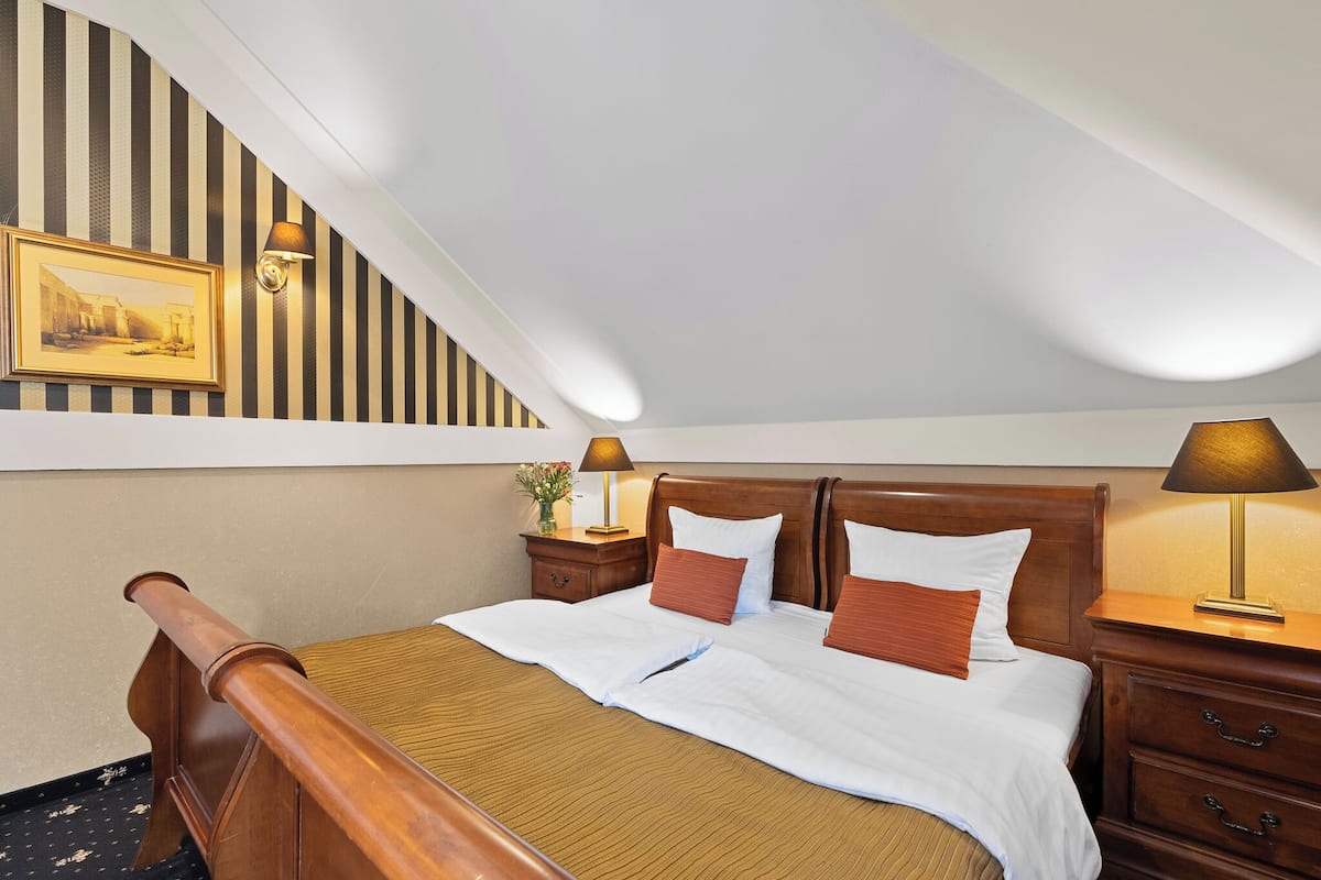A hotel room with a wooden bed, white bedding, a striped wall, and a painting.