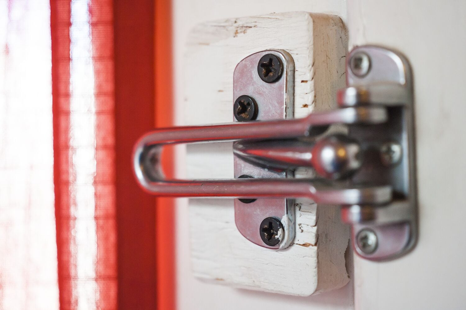 A close-up of a metal latch on a white door with a red frame.