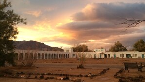 A desert landscape with a white building featuring a long corridor and small windows. - Amargosa Opera House (Death Valley)
