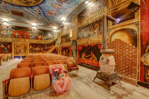 A theater with rows of wooden seats, a stage with a red curtain, and a large mural on the wall.