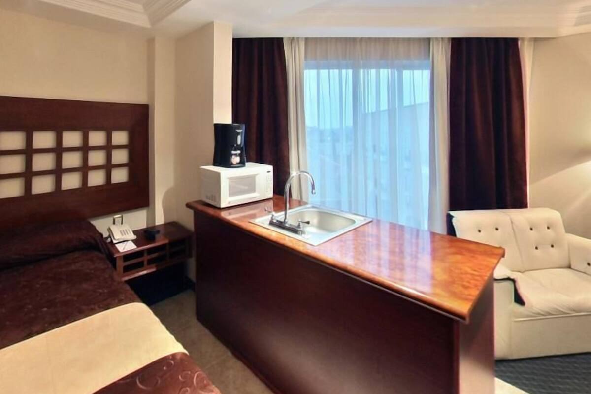 A hotel room with a bed, a desk with a coffee maker, a sink, and a chair.