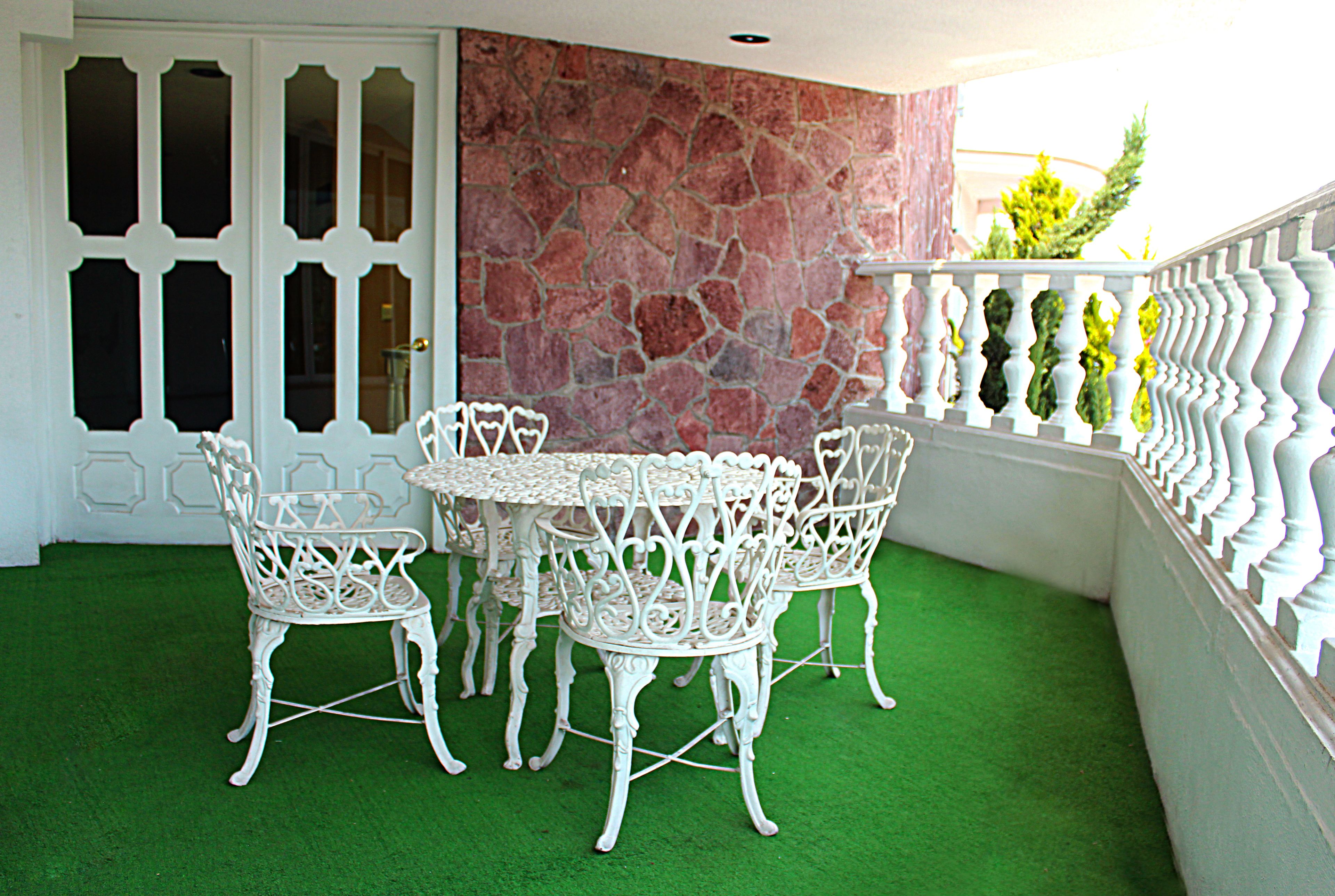 Eine Terrasse mit einer Steinsäule, weißen schmiedeeisernen Stühlen und einem runden Tisch.