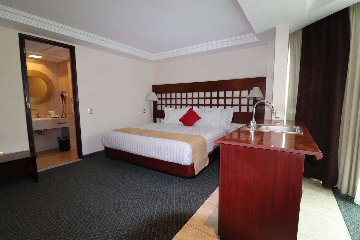 A hotel room with a bed, a wooden desk, a sink, and a mirror.