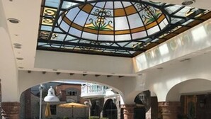 Um hall amplo com teto de vitrais, uma fonte central e vista para a rua.