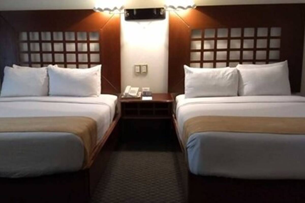 A hotel room with two single beds, a nightstand with a phone, and a wall-mounted light fixture.