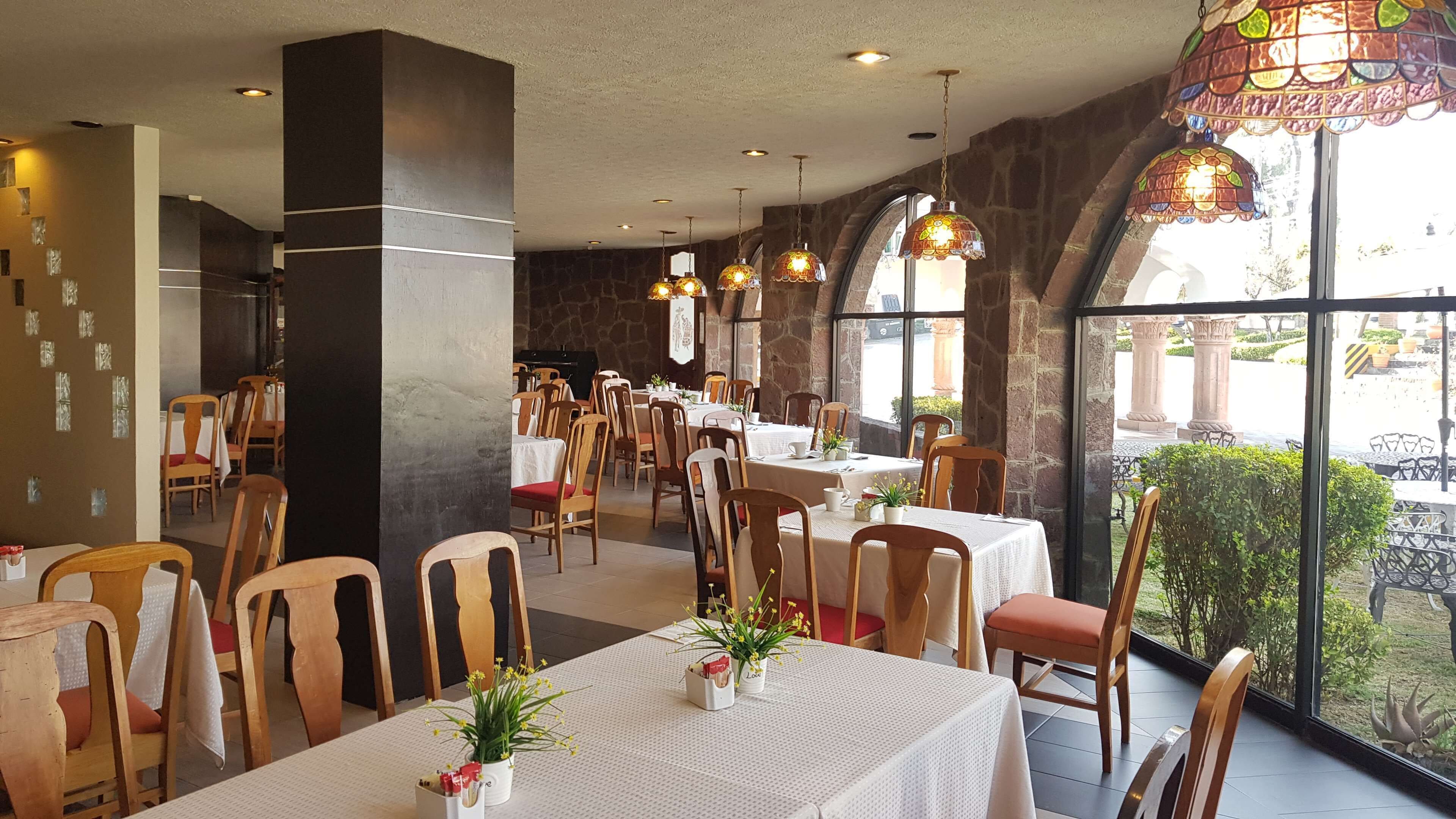 Een restaurant met verschillende tafels en stoelen, stenen muren en grote ramen met uitzicht op buiten.