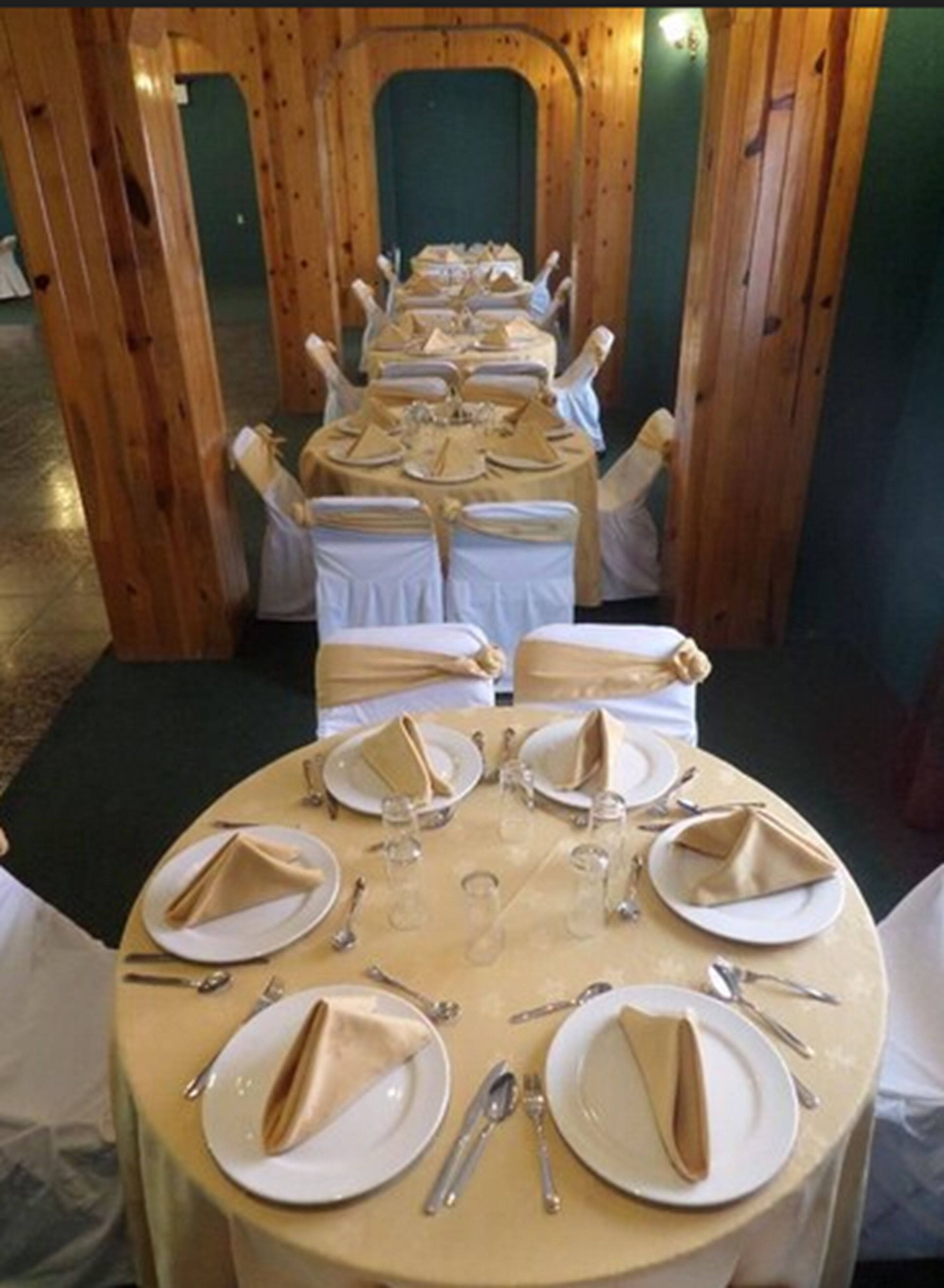 Una larga mesa dispuesta para un evento formal, con sillas blancas y servilletas dobladas en cada plato.