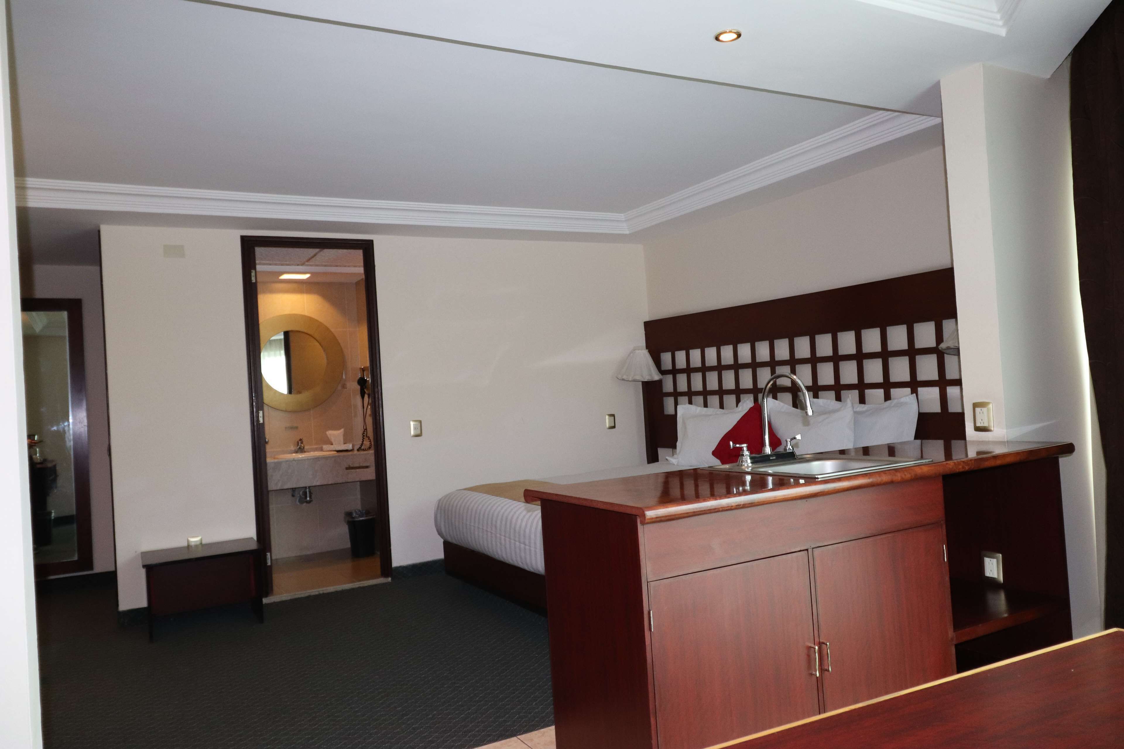 Ein Hotelzimmer mit einem Holztisch, einem Bett, einem Badezimmer mit Spiegel und Waschbecken.