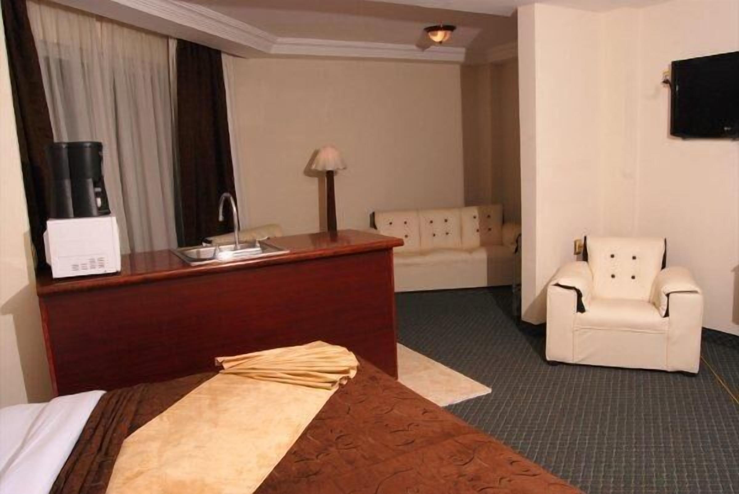Habitación de hotel con cama, escritorio con lámpara, silla y televisión en la pared.