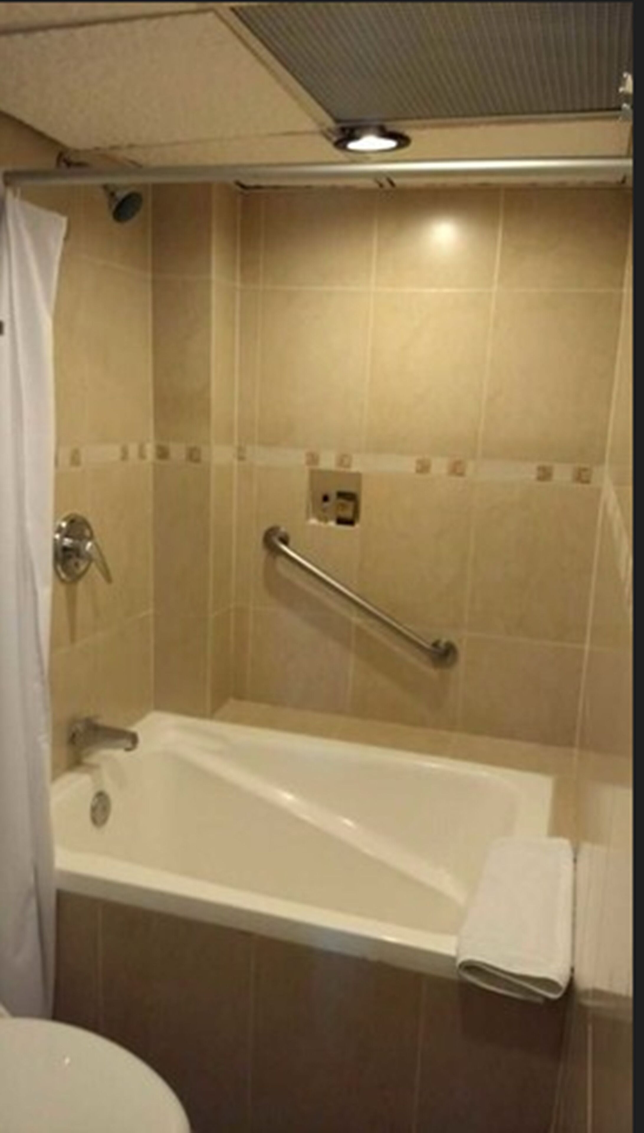 A bathroom with a bathtub, a handrail, and a shower curtain.