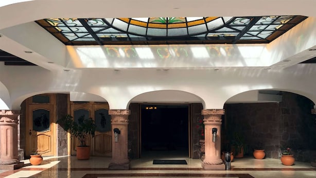 Um hall amplo com teto alto, um vitral e uma porta central ladeada por colunas.