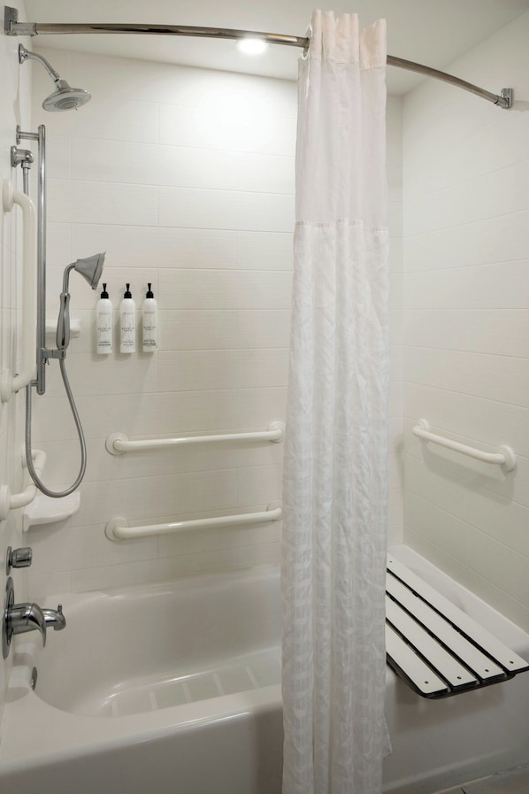 A white bathroom with a bathtub, shower, and handrails.