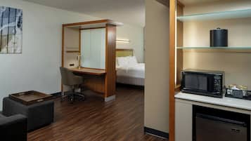A hotel room with a wooden floor, a bed with white linens, a desk with a chair, a microwave, and a small refrigerator.