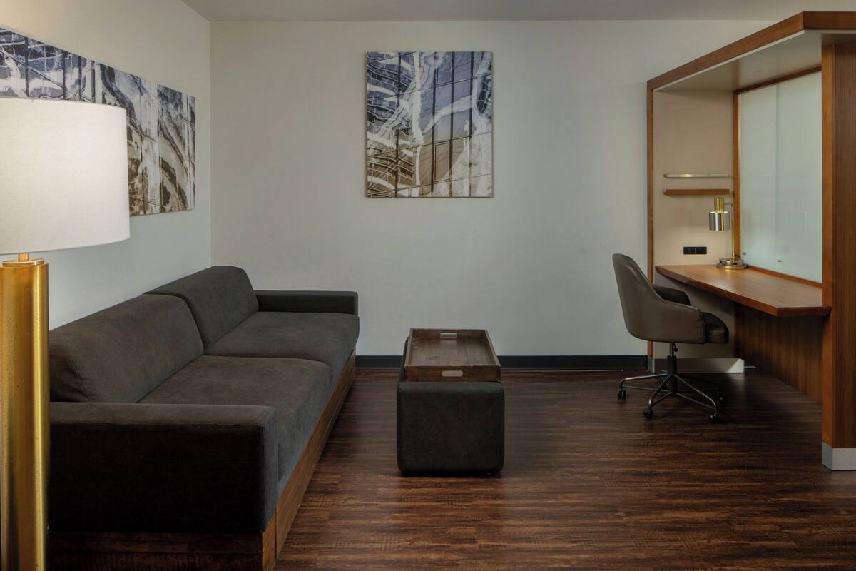 A modern room with a dark brown sofa, a small wooden side table, a desk with a chair, and two abstract paintings on the walls.