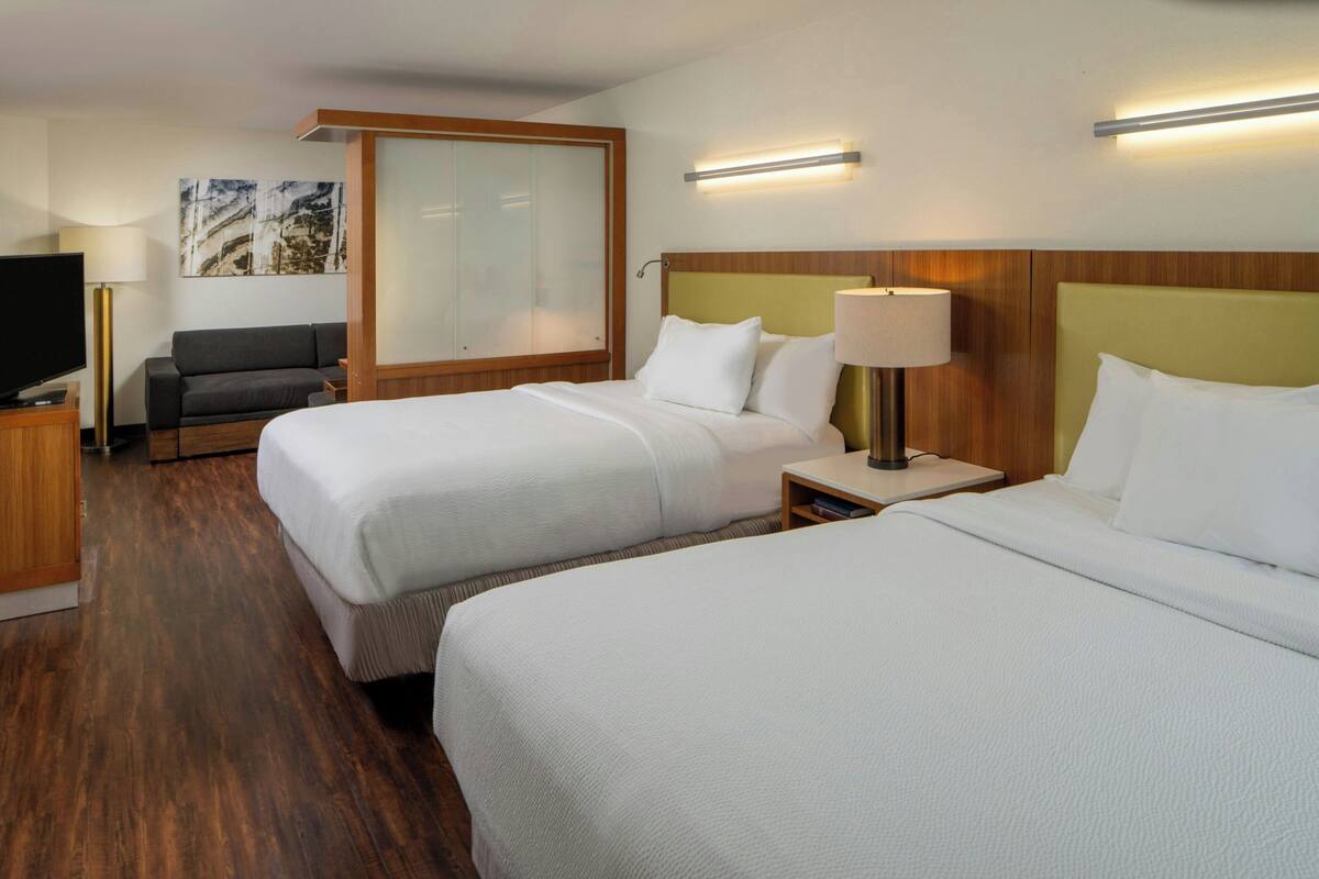 A hotel room with two beds, a sofa, a TV, and a painting on the wall.
