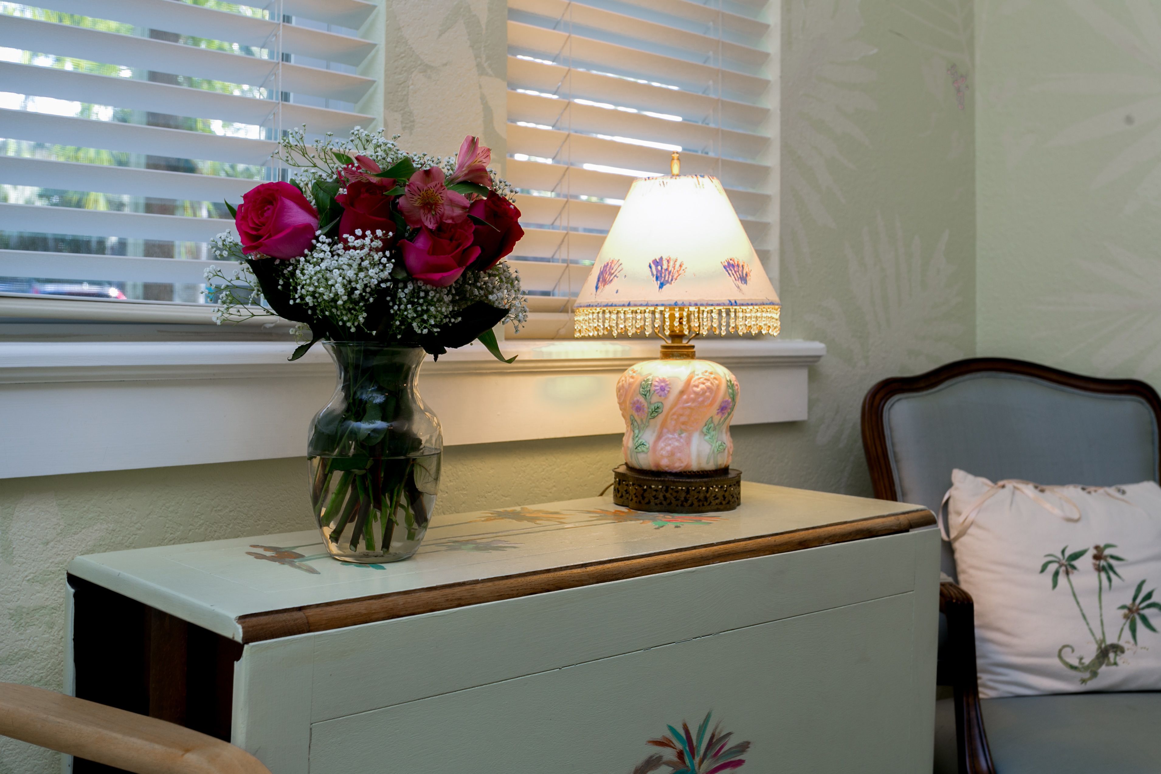 A bedside table with a vase of flowers and a lamp.