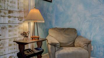 Una habitación con pared azul, un sillón color beige, una mesa con lámpara y un cuadro enmarco.