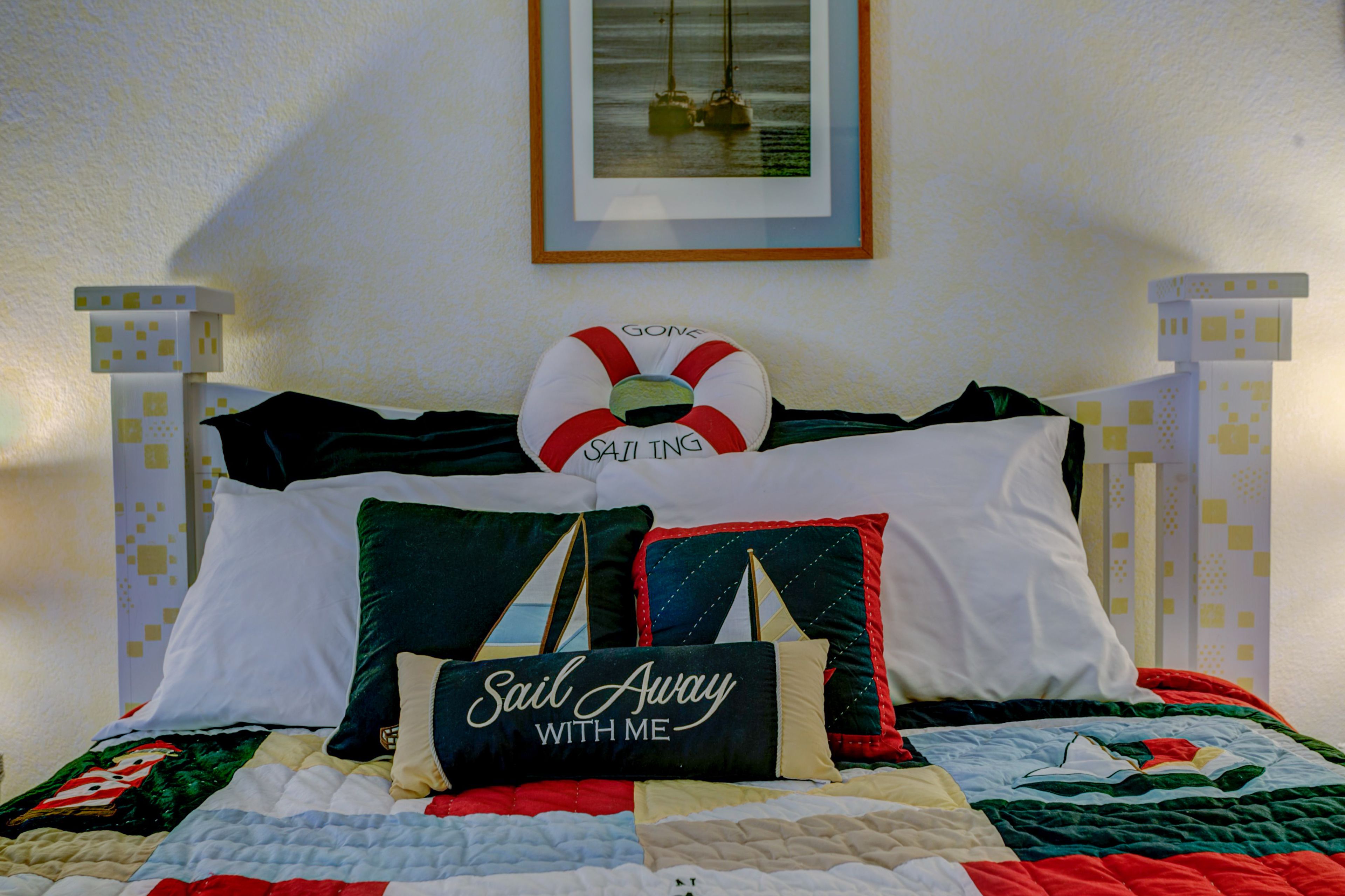 A bed with a quilt, pillows, and a framed picture on the wall.