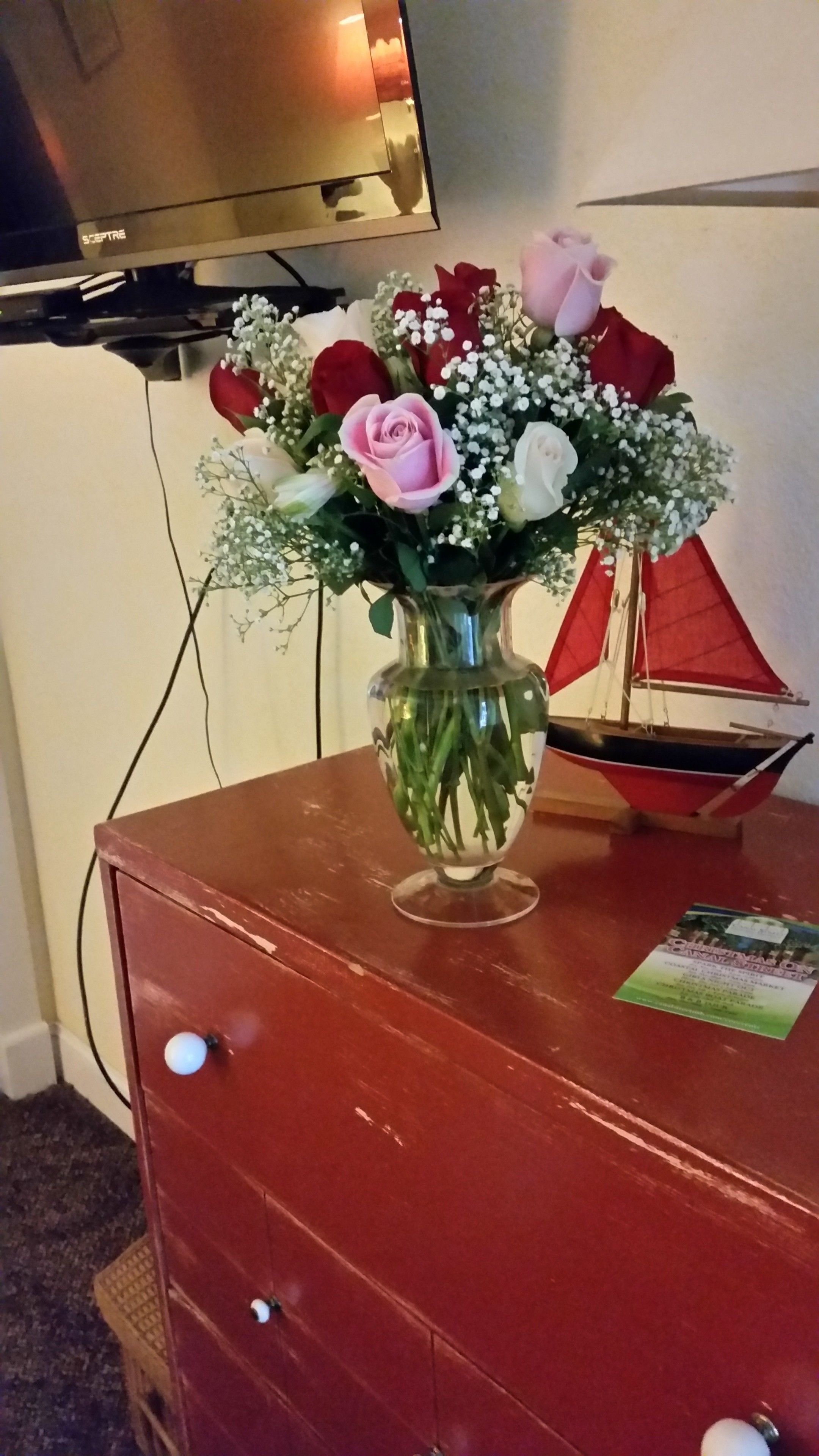 A wooden dresser with a vase of flowers and a small sailboat model on top.