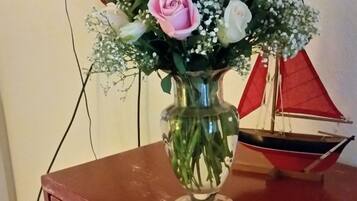 A wooden dresser with a vase of flowers and a small sailboat model on top.