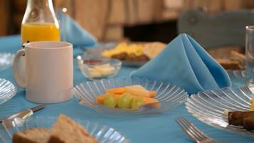A breakfast table with a white mug, a glass of orange juice, a plate with cheese and grapes, and a napkin folded on the table.
