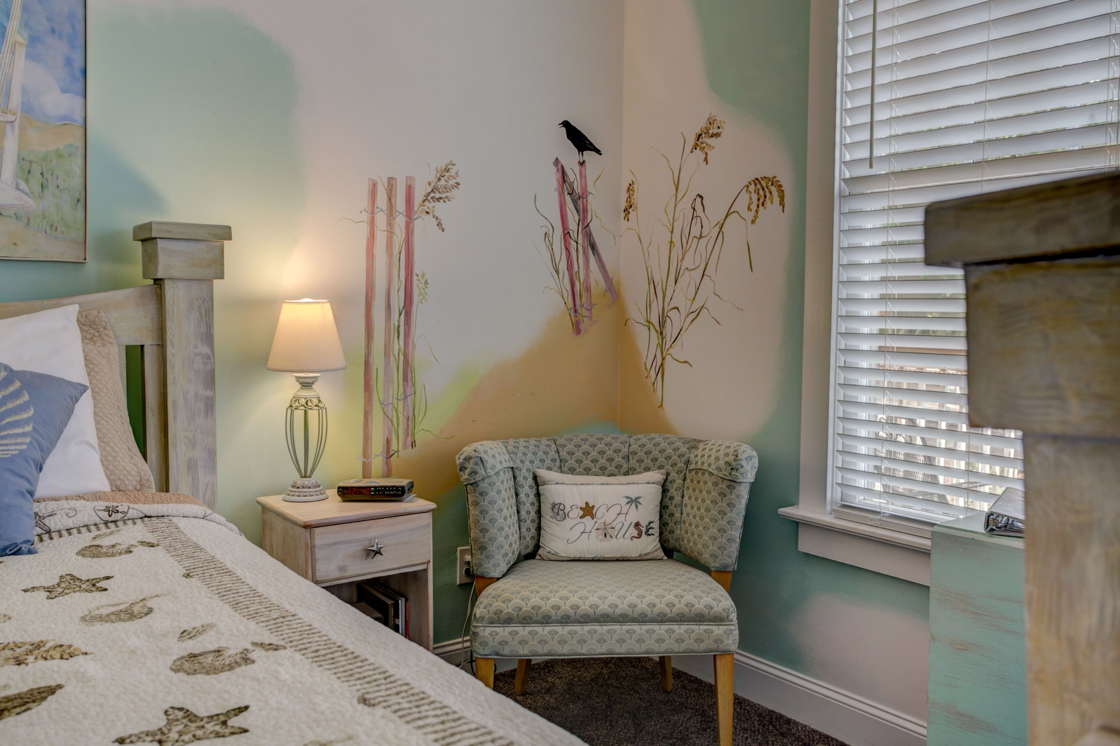 Une chambre à coucher comprenant un lit, une table de chevet, une lampe, une chaise et des œuvres d’art murales.