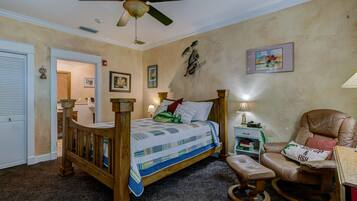 A bedroom with a wooden bed, a rocking chair, a ceiling fan, and a small bedside table with a lamp.